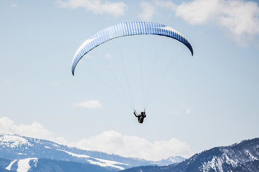 Paragleiter mit einem Blauen Schirm fliegt über den Alpen